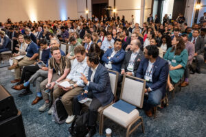 Attendees fill the ballroom, with some talking in the front rows.