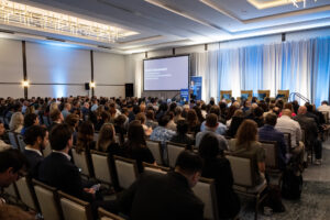 A full audience faces Emily Domenech on stage.