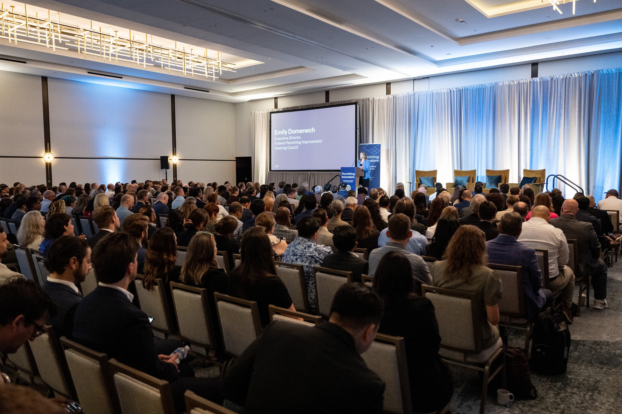 A full audience faces Emily Domenech on stage.