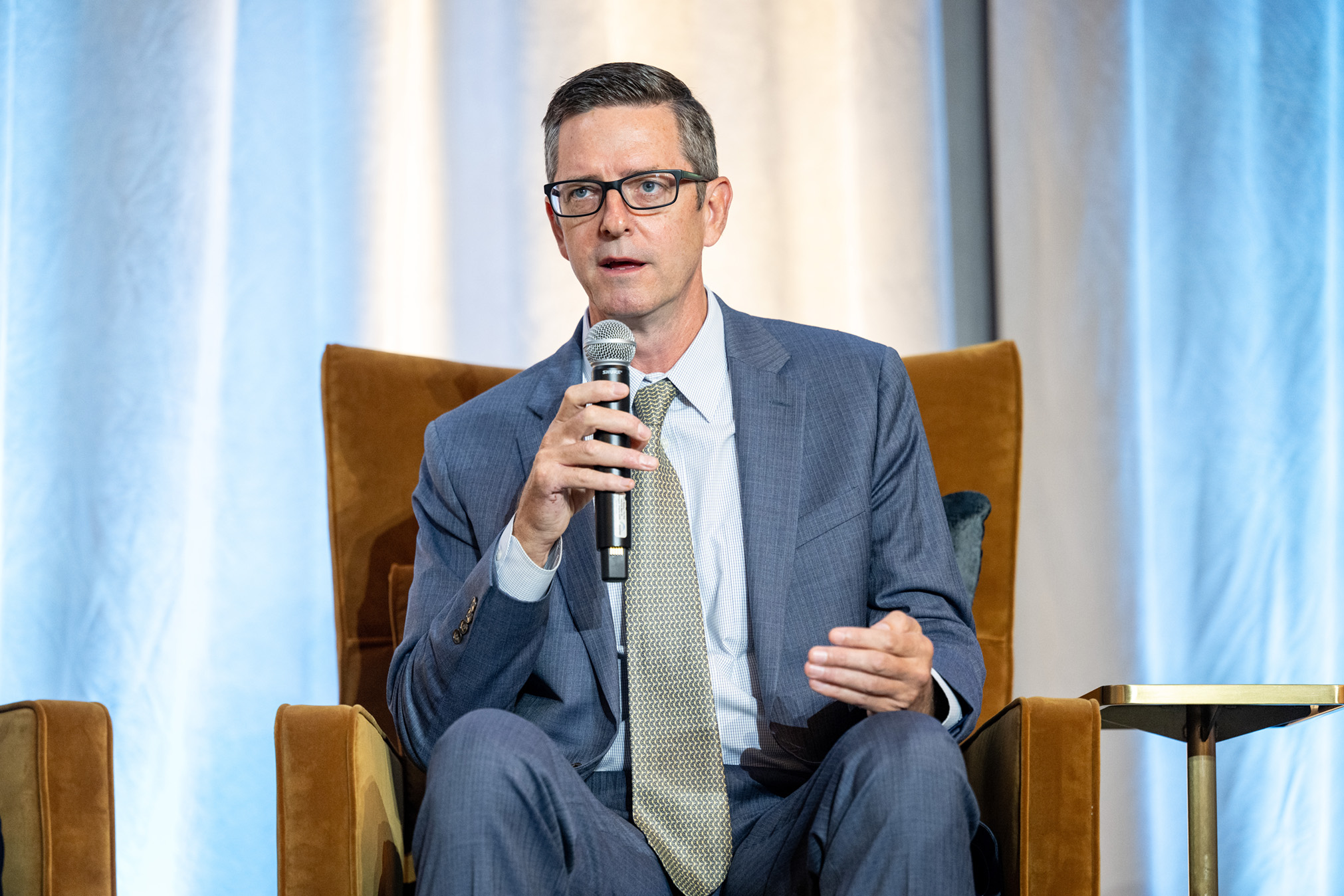 Chad Whiteman gestures while speaking into a microphone on stage.