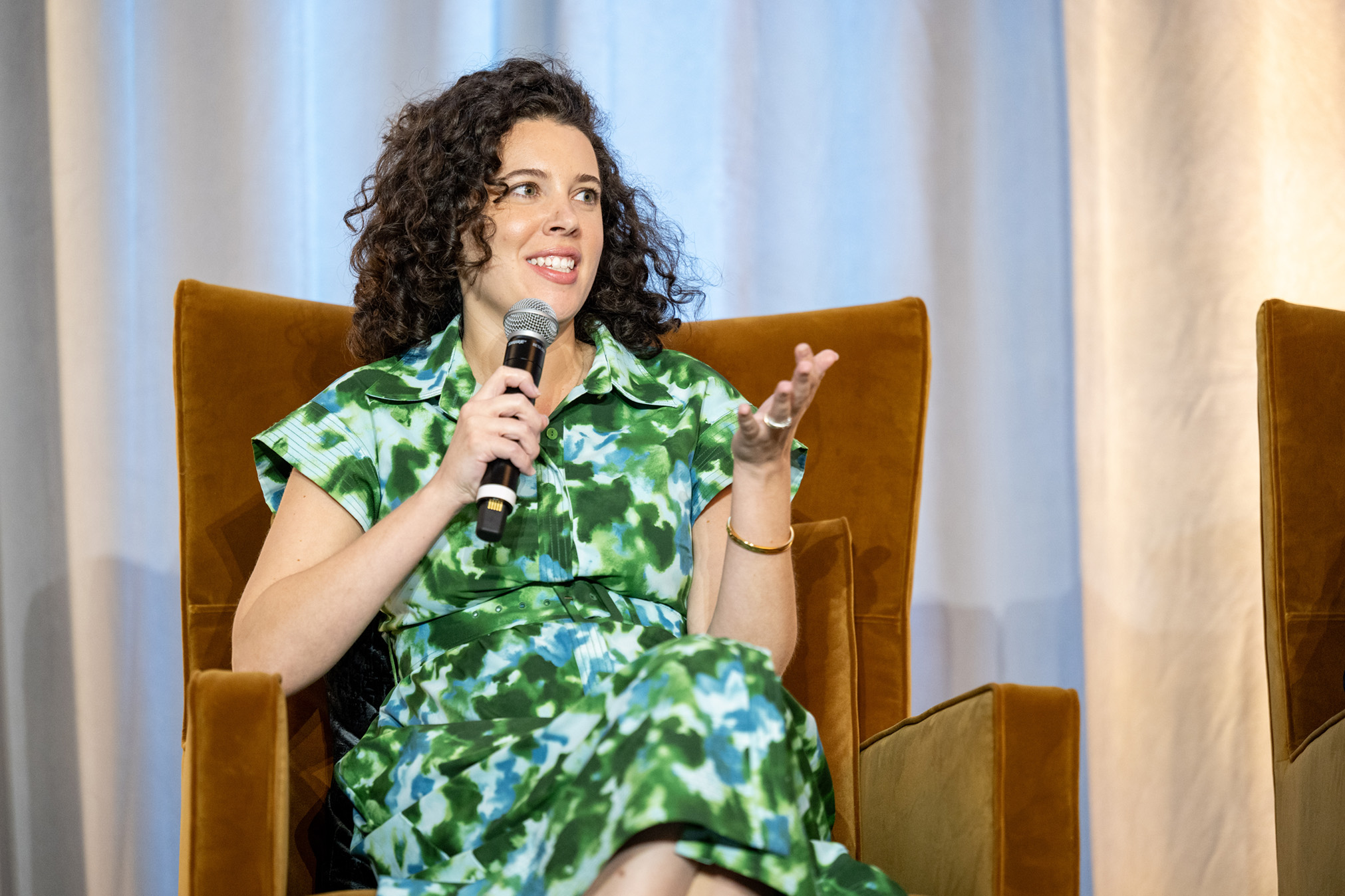 Maggie Ayrea gestures while speaking into a microphone on stage.