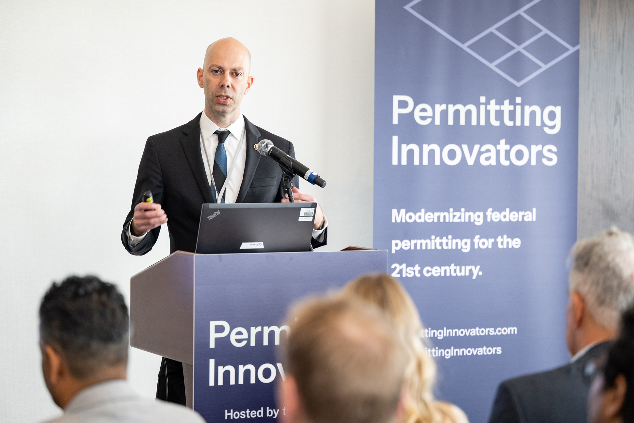 Jordan Eccles points toward the audience with a slide remote while speaking at the lectern.