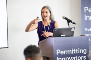 Elizabeth Ayer gestures toward the audience while presenting at the lectern.